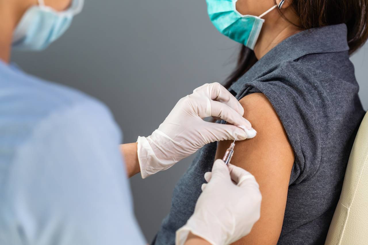 Frau mit medizinischer Maske wird in den Oberarm geimpft
